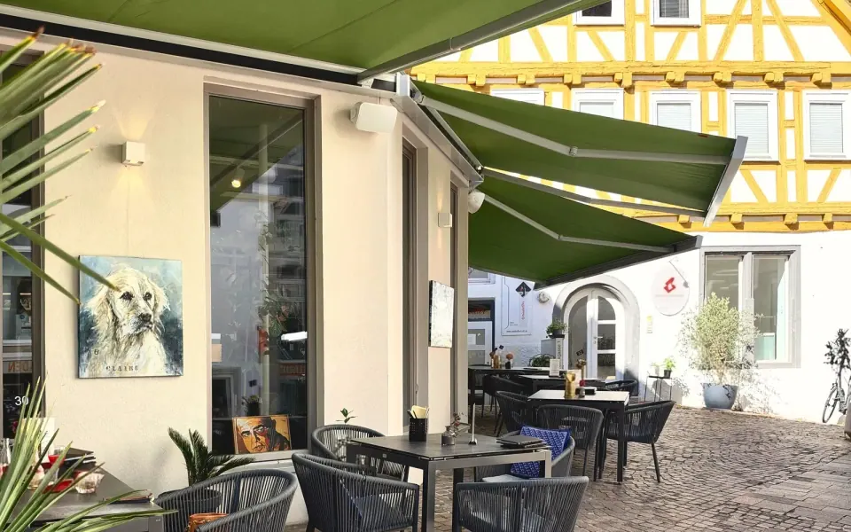 Die Außenterrasse unter grünen Markisen, dahinter Fachwerkhäuser am Marktplatz