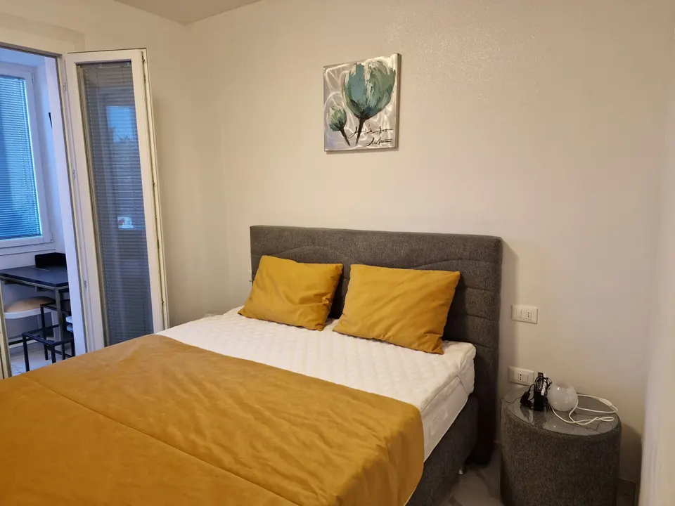 Schlafzimmer mit Doppelbett, grauem Kopfteil und senfgelben Kissen