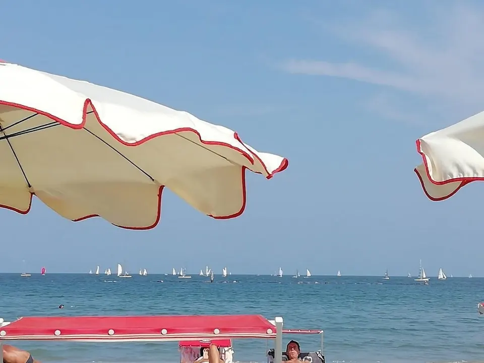 Sonnenschirme am Strand, Segelboote am Horizont