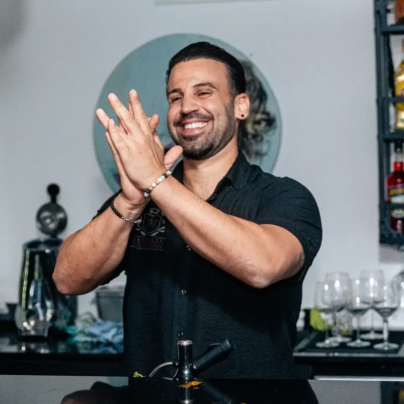 Giorgio lacht hinter der Bar und klatscht in die Hände, dahinter das Regal mit Aperol und Prosecco