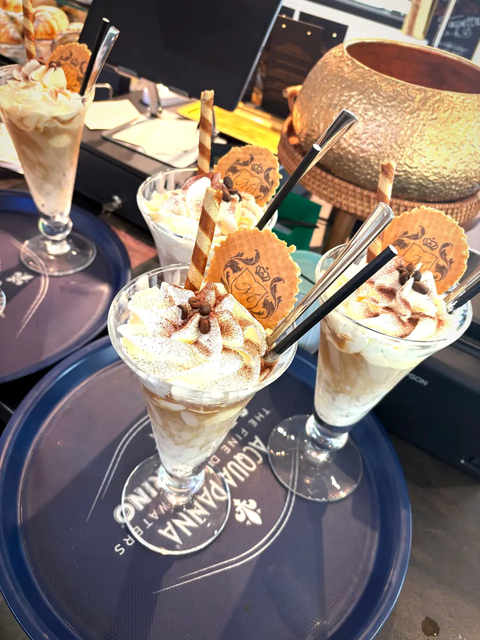 Vier Gläser Eiskaffee mit Sahne und Keks auf einem Tablett an der Theke
